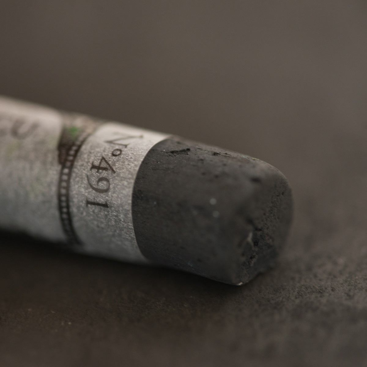 A close-up of a dark brown Sennelier extra soft pastel. on the same coloured background, with the colour information printed on the paper wrap.