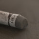 A close-up of a brown Sennelier extra soft pastel. on the same coloured background, with the colour information printed on the paper wrap.