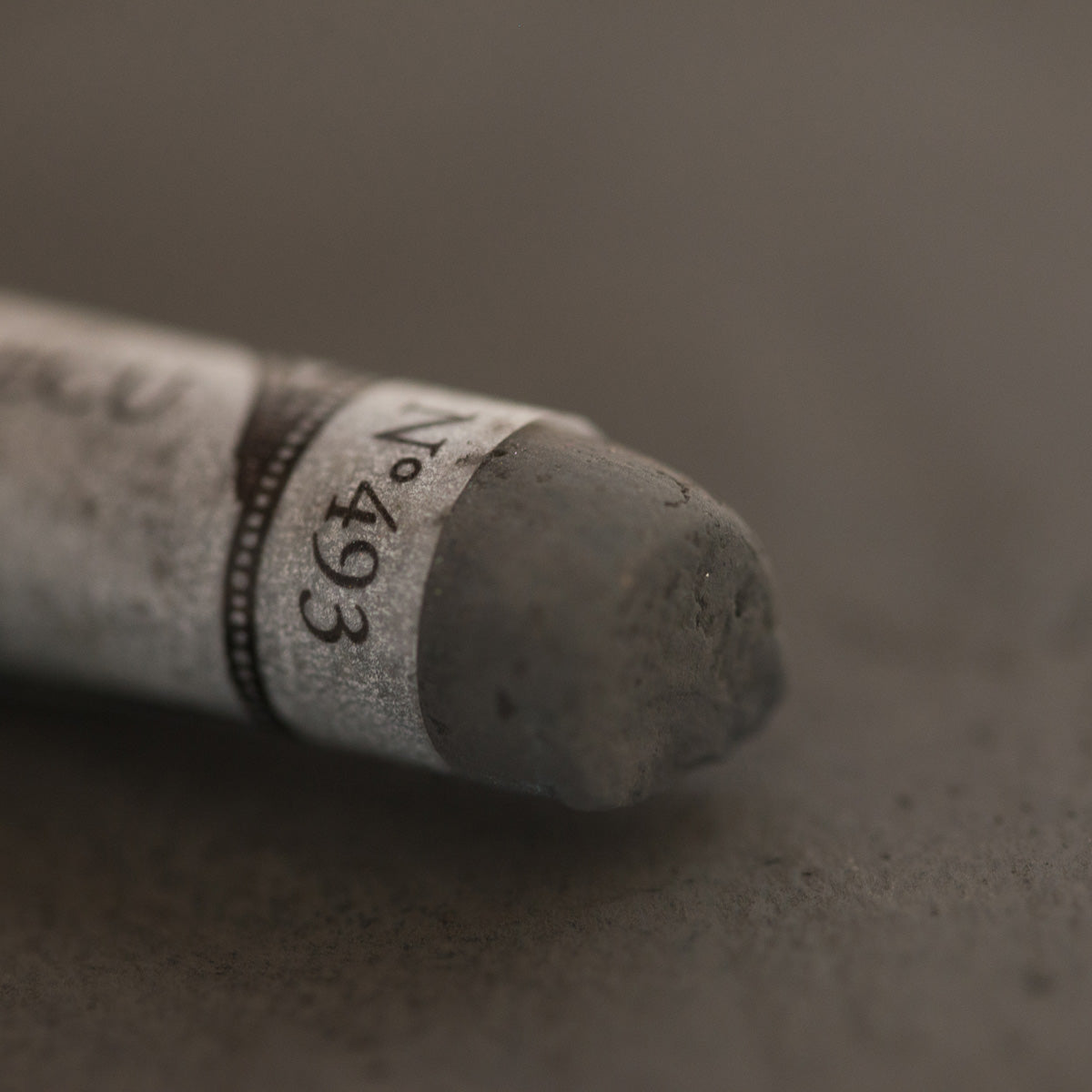A close-up of a brown Sennelier extra soft pastel. on the same coloured background, with the colour information printed on the paper wrap.