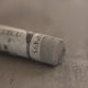 A close-up of a grey Sennelier extra soft pastel. on the same coloured background, with the colour information printed on the paper wrap.