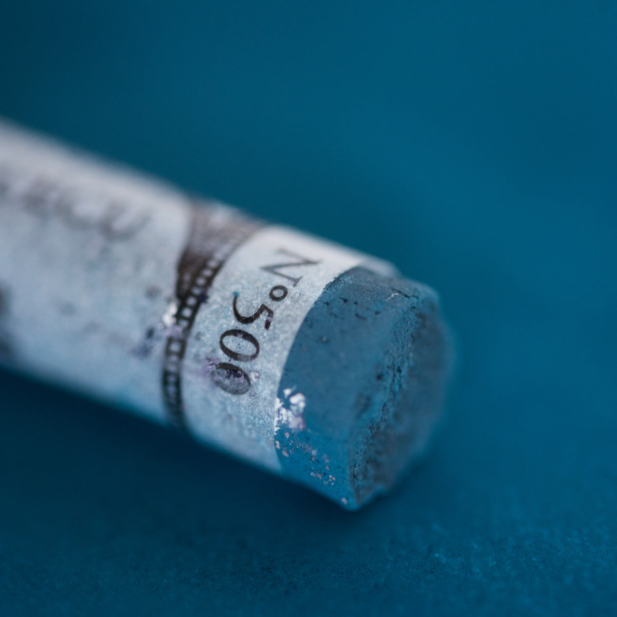 A close-up of deep blue Sennelier extra soft pastel. on the same coloured background, with the colour information printed on the paper wrap.