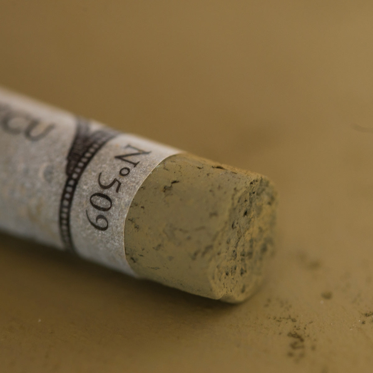 A close-up of a brown Sennelier extra soft pastel. on the same coloured background, with the colour information printed on the paper wrap.