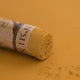 A close-up of a ochre Sennelier extra soft pastel. on the same coloured background, with the colour information printed on the paper wrap.