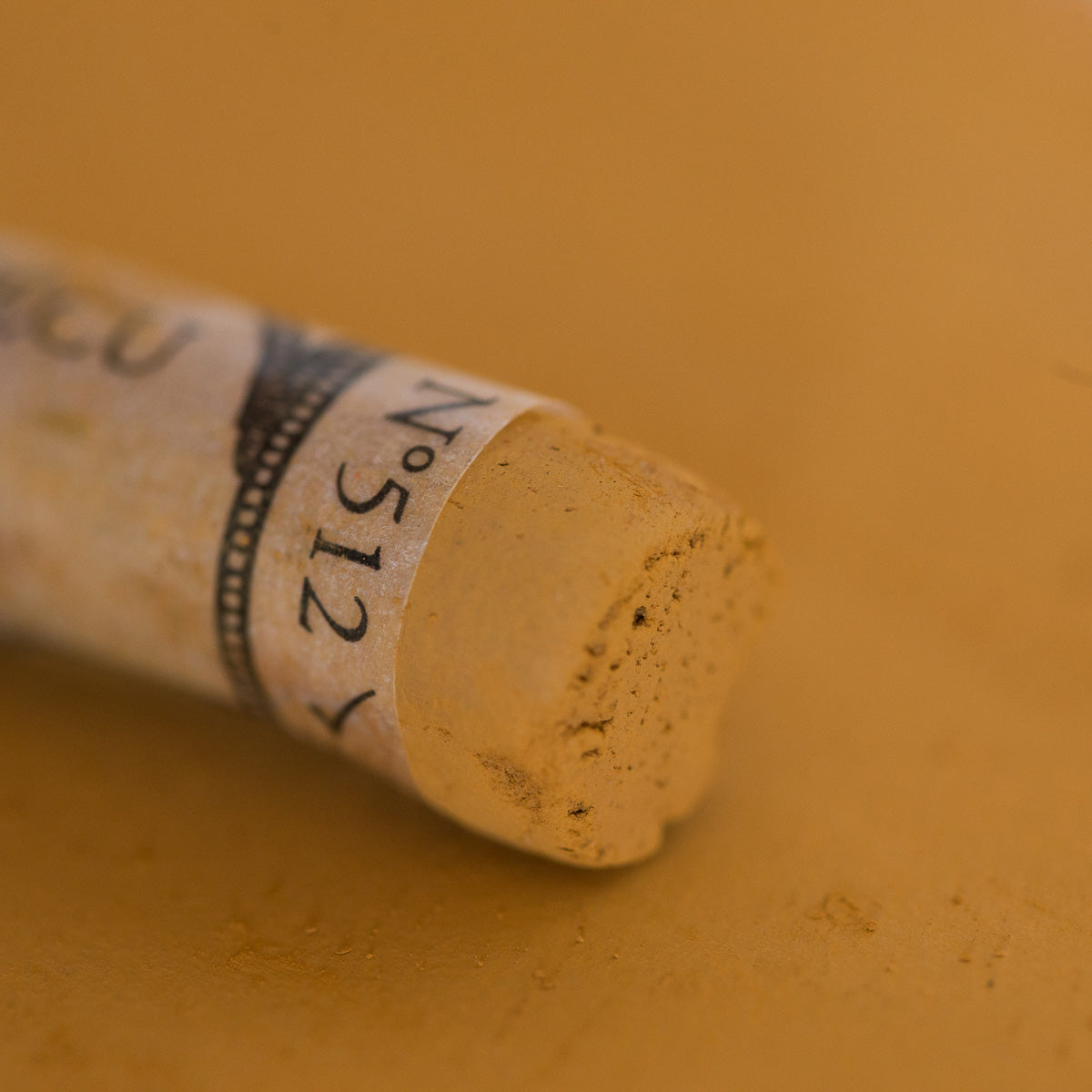 A close-up of a brown Sennelier extra soft pastel. on the same coloured background, with the colour information printed on the paper wrap.