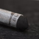A close-up of a black Sennelier extra soft pastel. on the same coloured background, with the colour information printed on the paper wrap.