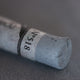 A close-up of a grey Sennelier extra soft pastel. on the same coloured background, with the colour information printed on the paper wrap.