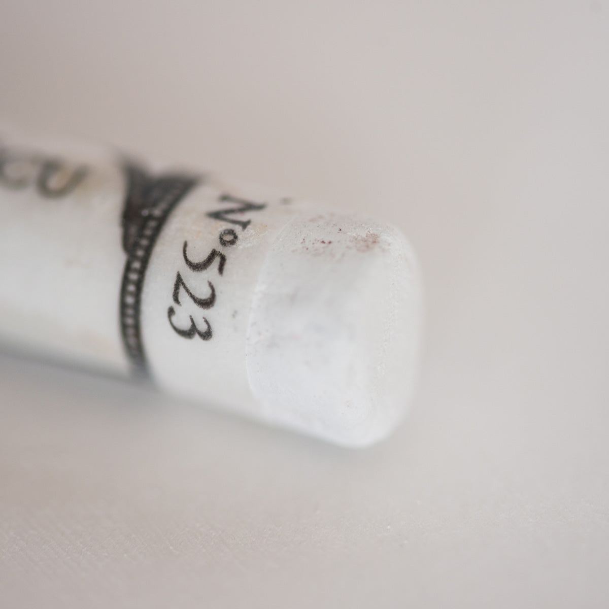 A close-up of a white Sennelier extra soft pastel. on the same coloured background, with the colour information printed on the paper wrap.