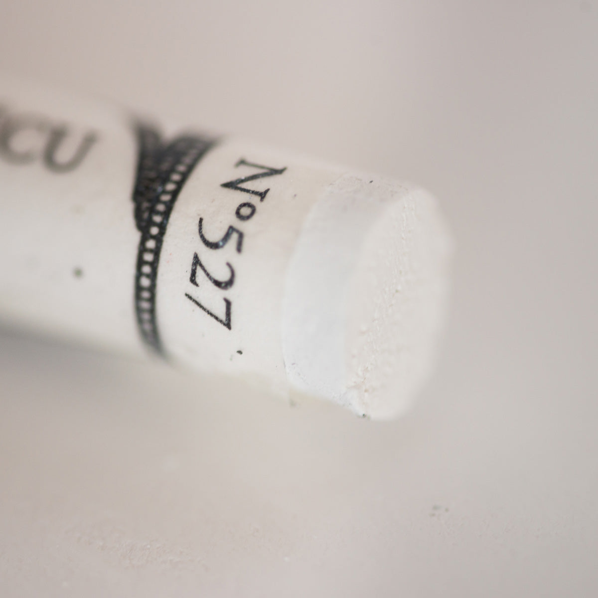 A close-up of a white Sennelier extra soft pastel. on the same coloured background, with the colour information printed on the paper wrap.