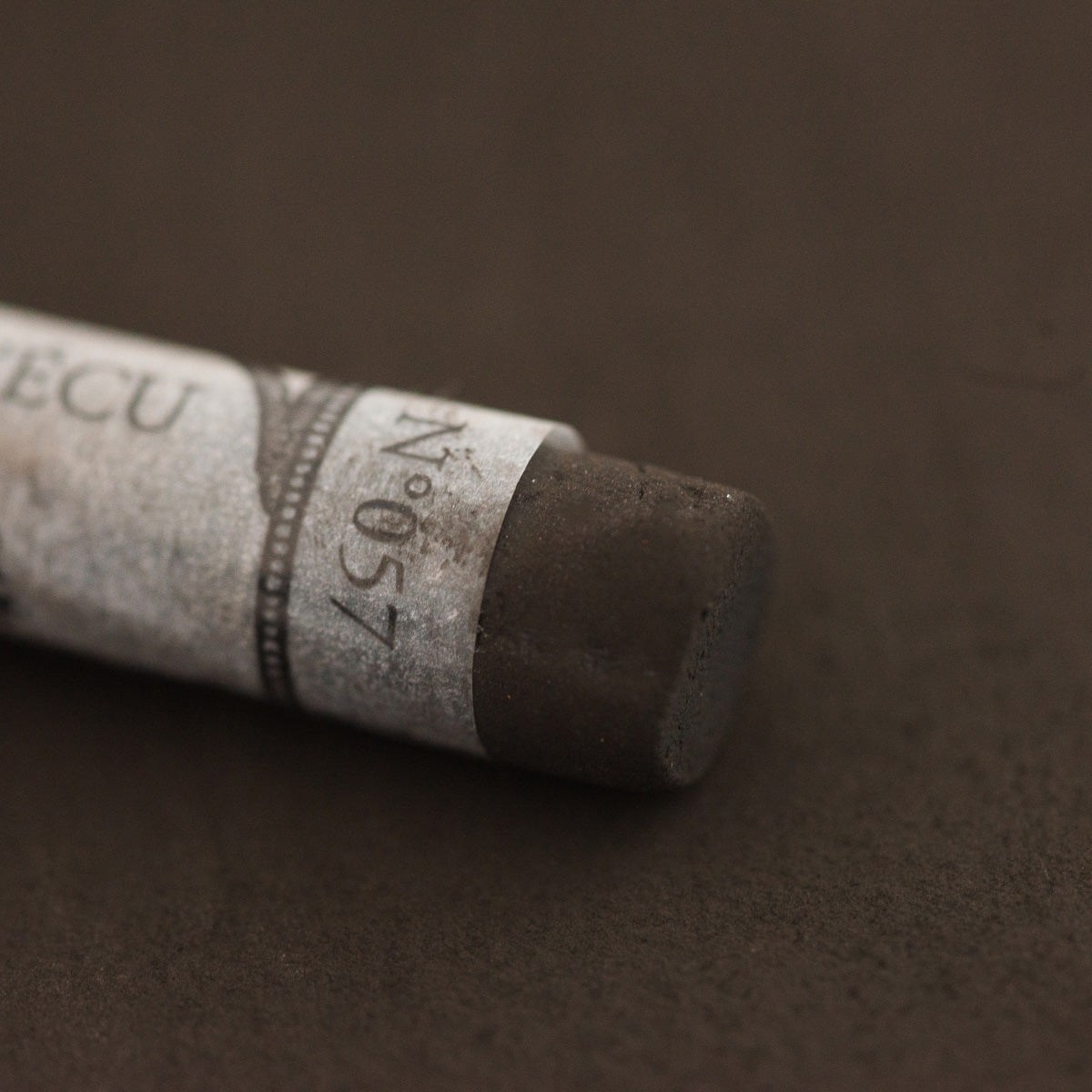 A close-up of a brown Sennelier extra soft pastel with the colour information printed on the paper wrap.