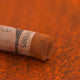 A close-up of a brown Sennelier extra soft pastel with the colour information printed on the paper wrap.