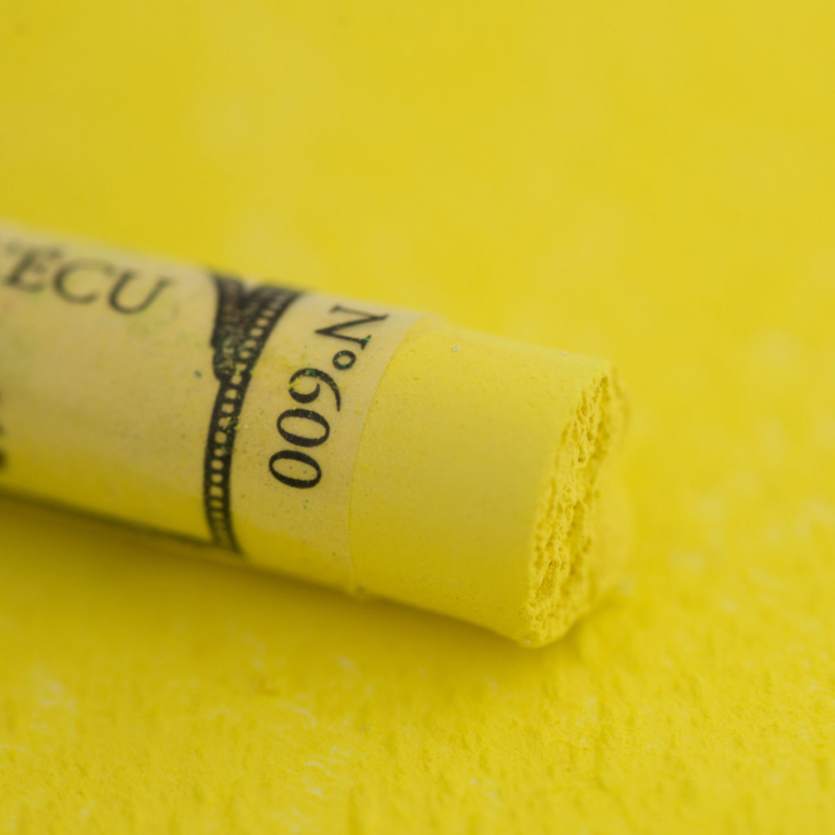 A close-up of a yellow Sennelier extra soft pastel. on the same coloured background, with the colour information printed on the paper wrap.