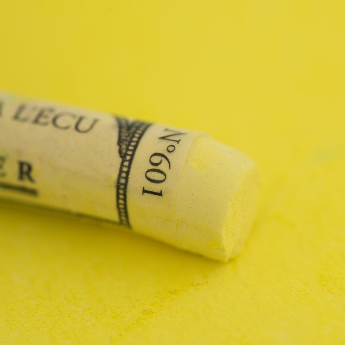 A close-up of a yellow Sennelier extra soft pastel. on the same coloured background, with the colour information printed on the paper wrap.