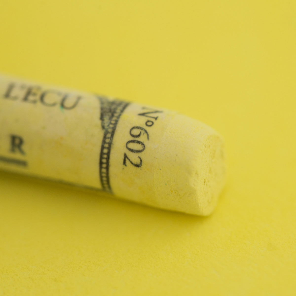 A close-up of a yellow Sennelier extra soft pastel. on the same coloured background, with the colour information printed on the paper wrap.