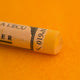 A close-up of an Orange Sennelier extra soft pastel. on the same coloured background, with the colour information printed on the paper wrap.