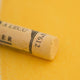 A close-up of a yellow Sennelier extra soft pastel. on the same coloured background, with the colour information printed on the paper wrap.