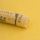 A close-up of a yellow Sennelier extra soft pastel. on the same coloured background, with the colour information printed on the paper wrap.