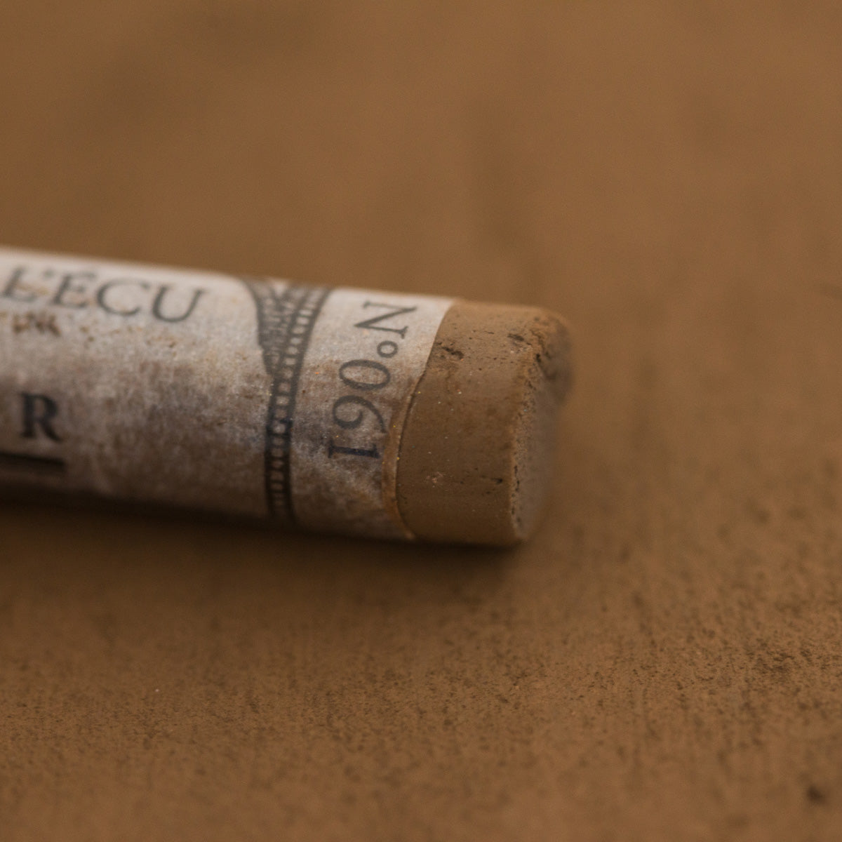 A close-up of a brown Sennelier extra soft pastel with the colour information printed on the paper wrap.