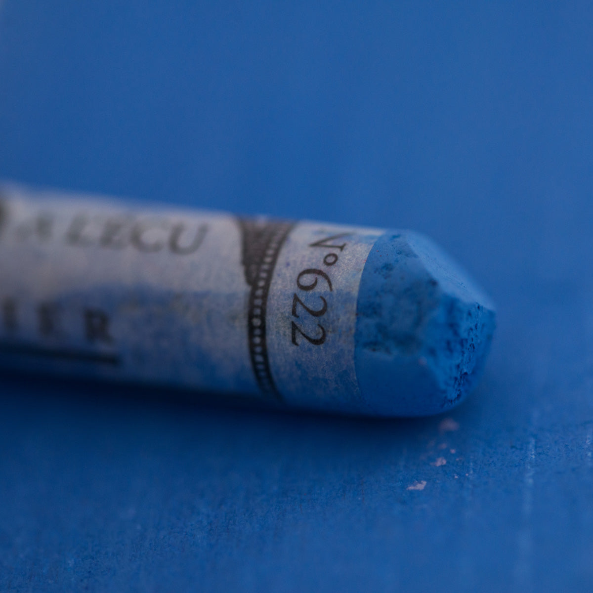  A close-up of a blue Sennelier extra soft pastel on the same coloured background, with the colour information printed on the paper wrap.