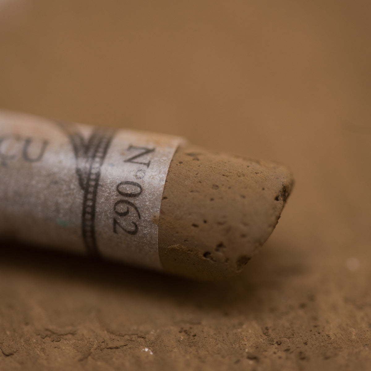 A close-up of a brown Sennelier extra soft pastel with the colour information printed on the paper wrap.