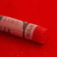 A close-up of a red Sennelier extra soft pastel on the same coloured background, with the colour information printed on the paper wrap.