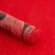 A close-up of a red Sennelier extra soft pastel on the same coloured background, with the colour information printed on the paper wrap.