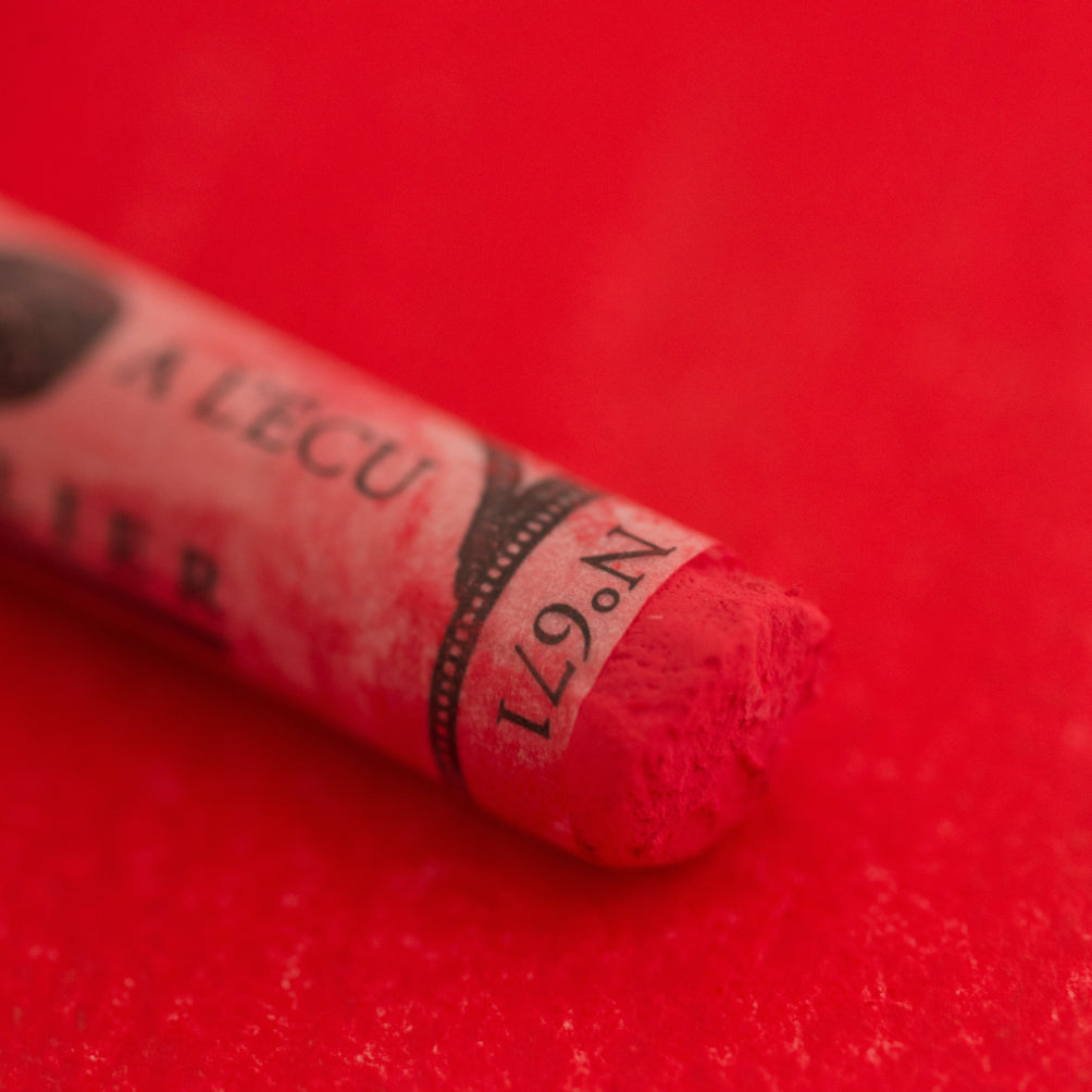 A close-up of a red Sennelier extra soft pastel on the same coloured background, with the colour information printed on the paper wrap.