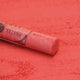 A close-up of a red Sennelier extra soft pastel. on the same coloured background, with the colour information printed on the paper wrap.