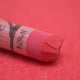 A close-up of a red Sennelier extra soft pastel. on the same coloured background, with the colour information printed on the paper wrap.