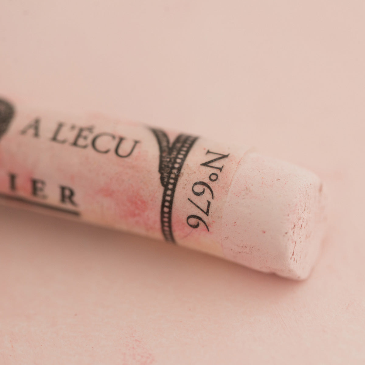 A close-up of a white Sennelier extra soft pastel. on the same coloured background, with the colour information printed on the paper wrap.
