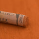 A close-up of a Sennelier extra soft pastel on a brown background with the colour information printed on the paper wrap.