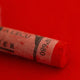 A close-up of a red Sennelier extra soft pastel on the same coloured background, with the colour information printed on the paper wrap.