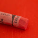 A close-up of a red Sennelier extra soft pastel on the same coloured background, with the colour information printed on the paper wrap.