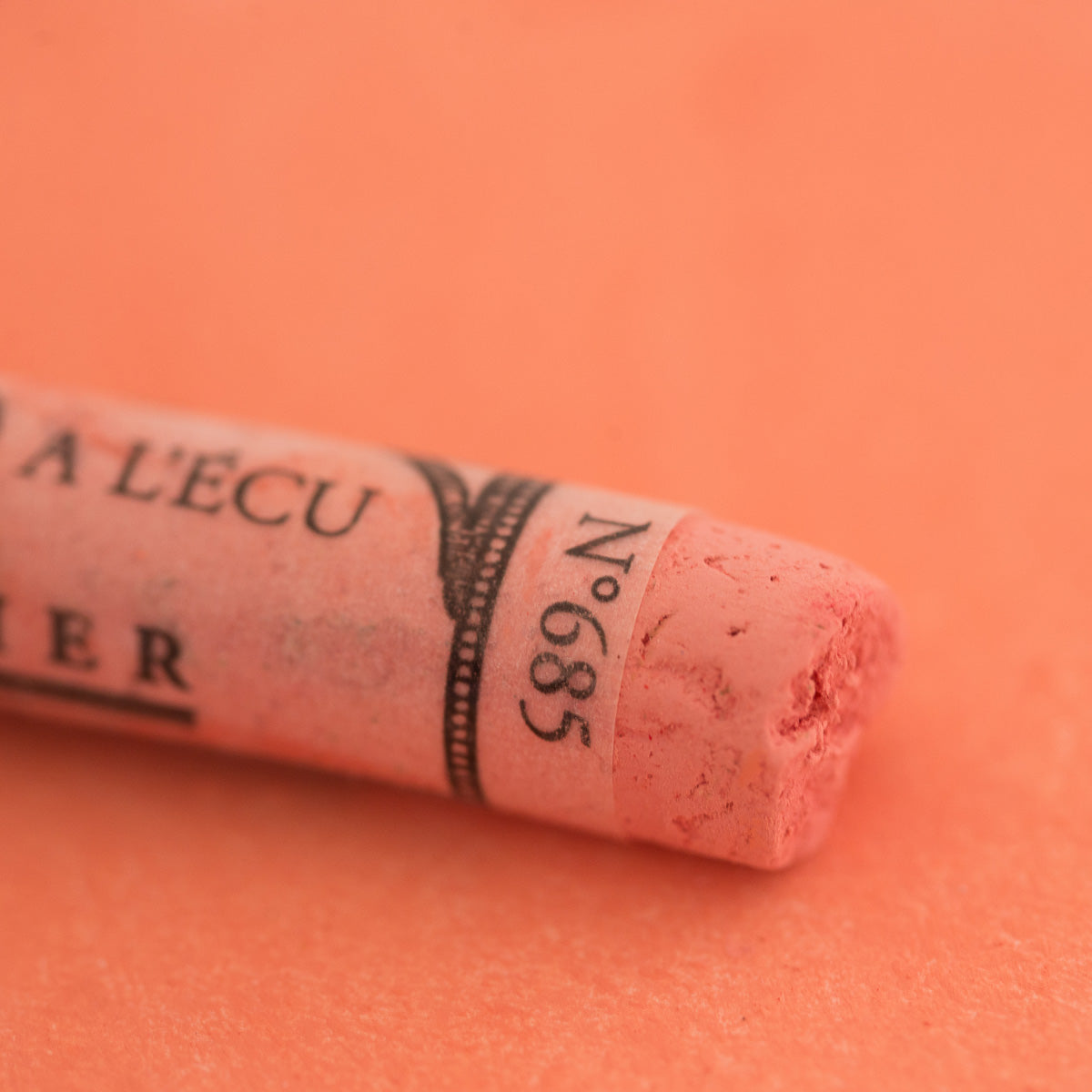 A close-up of a light red Sennelier extra soft pastel on the same coloured background, with the colour information printed on the paper wrap.