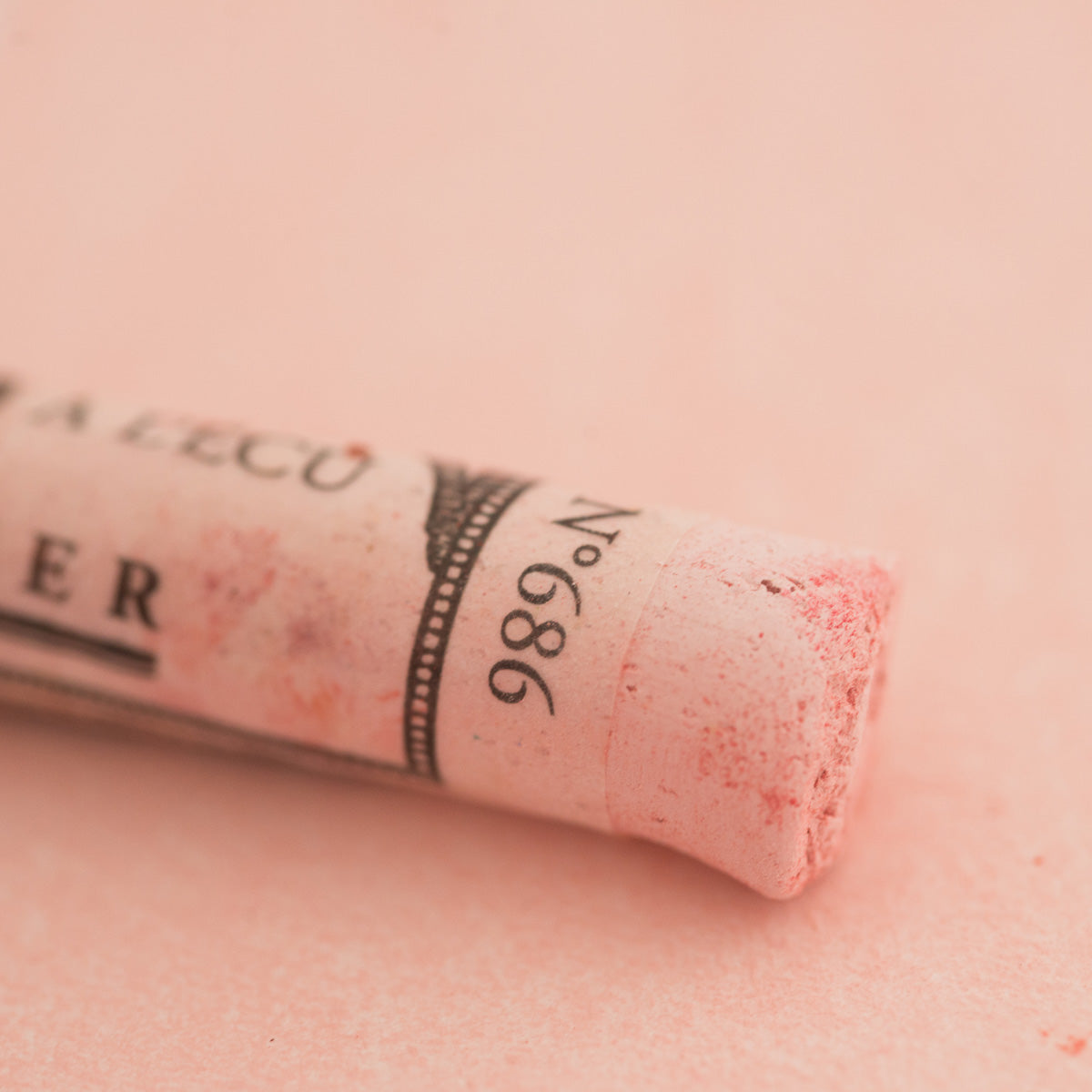 A close-up of a pale red Sennelier extra soft pastel on the same coloured background, with the colour information printed on the paper wrap.