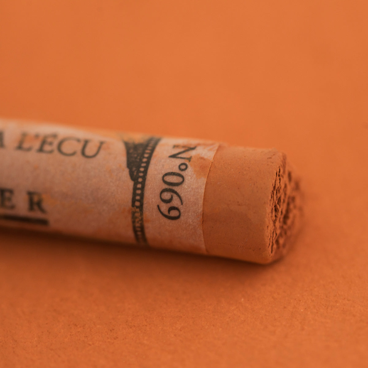 A close-up of a Sennelier extra soft pastel on a rusty brown background with the colour information printed on the paper wrap.