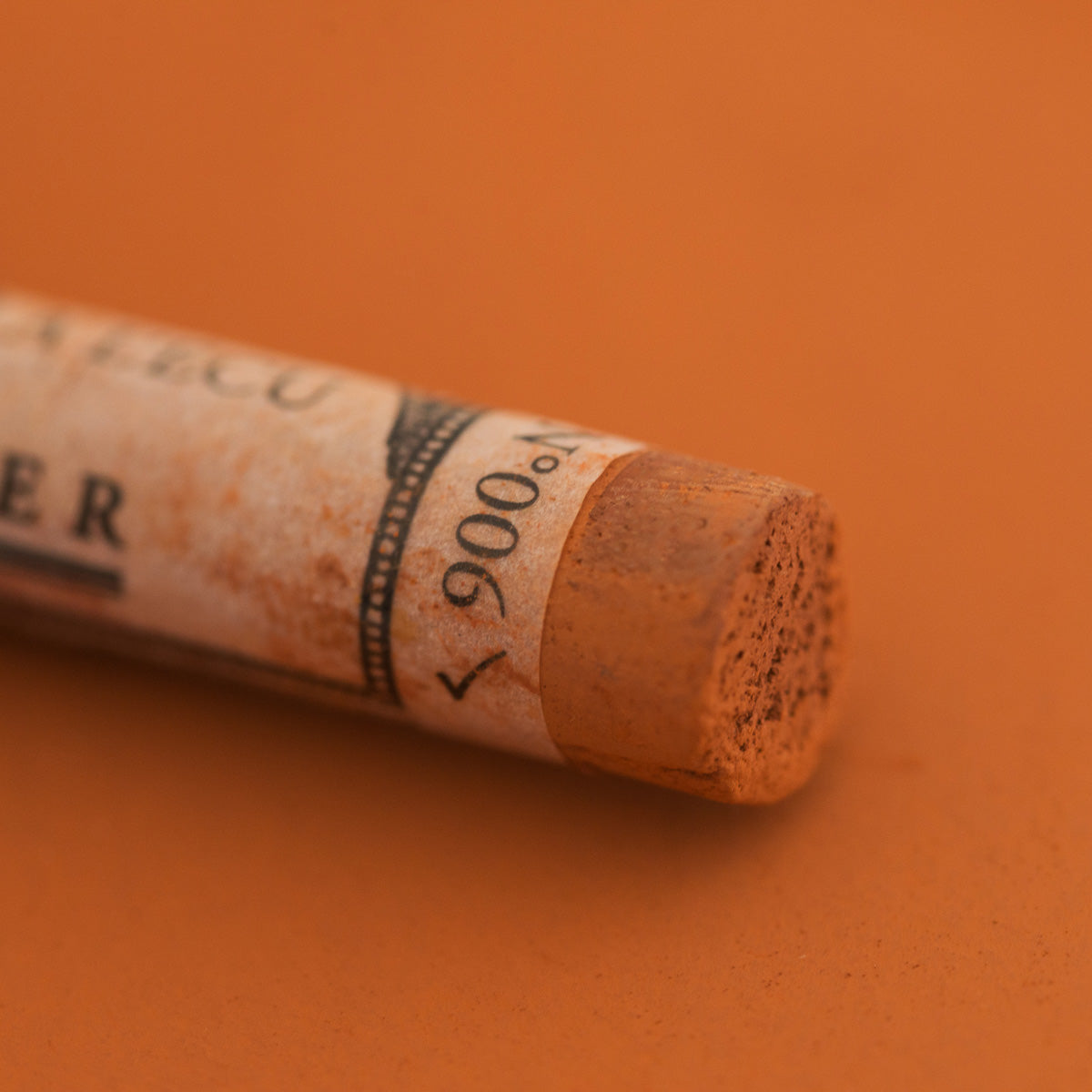 A close-up of a Sennelier extra soft pastel on a brown background with the colour information printed on the paper wrap.