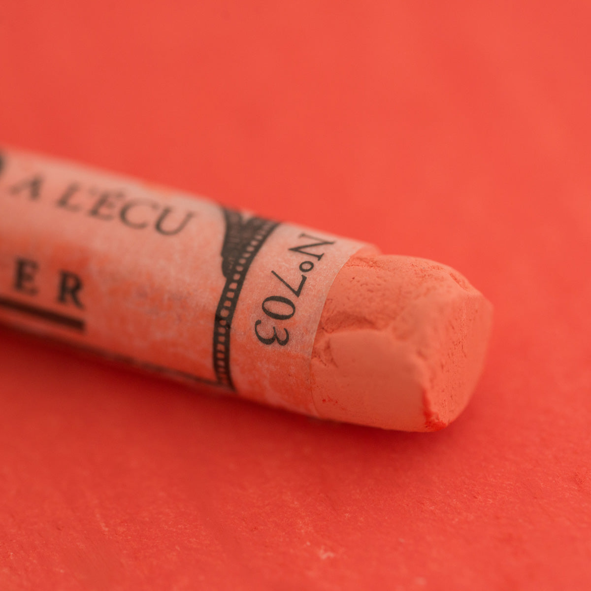 A close-up of a red Sennelier extra soft pastel on the same coloured background, with the colour information printed on the paper wrap.