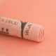 A close-up of a soft red Sennelier extra soft pastel on the same coloured background, with the colour information printed on the paper wrap.