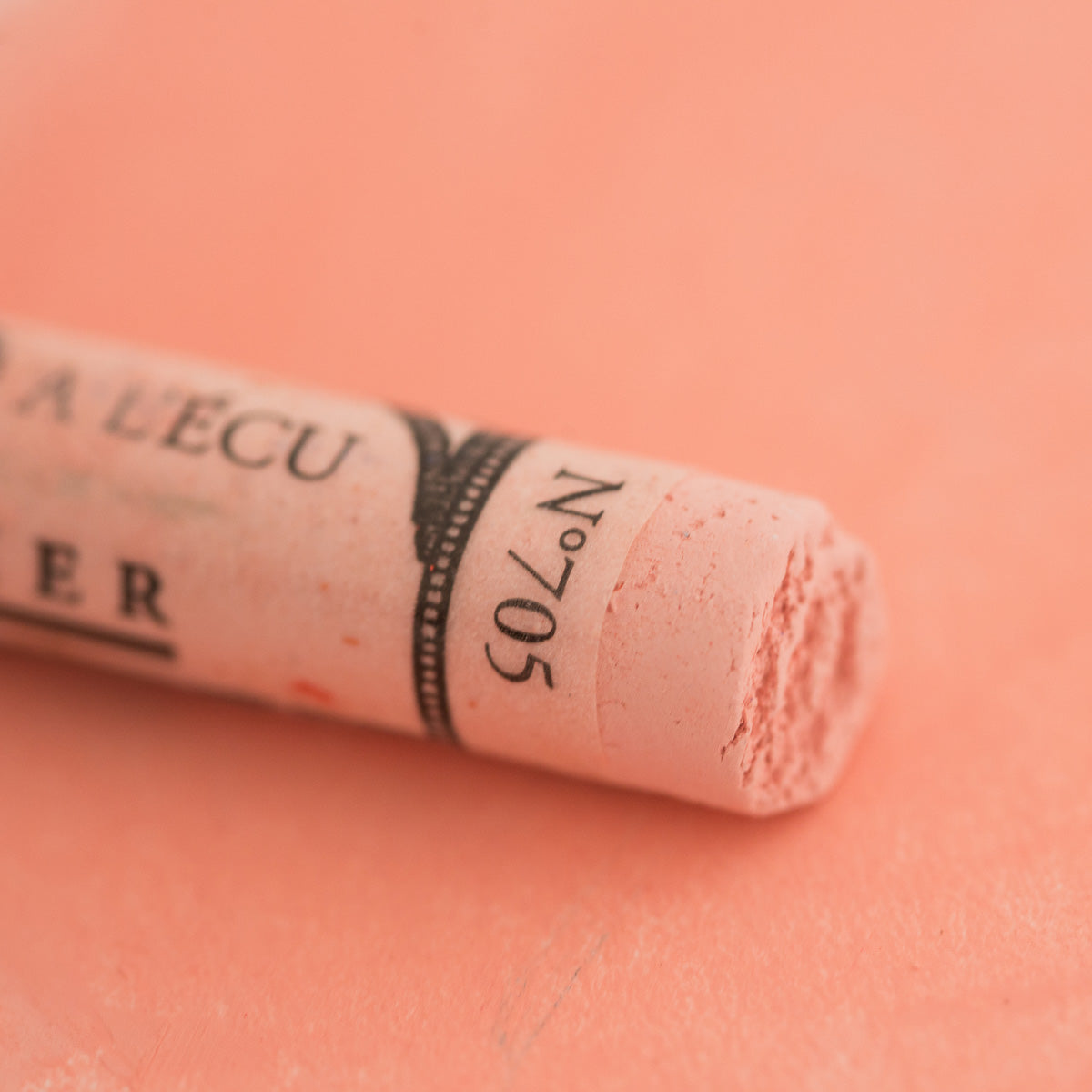 A close-up of a soft red Sennelier extra soft pastel on the same coloured background, with the colour information printed on the paper wrap.