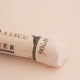 A close-up of a white Sennelier extra soft pastel on the same coloured background, with the colour information printed on the paper wrap.