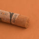 A close-up of a Sennelier extra soft pastel on a light brown background with the colour information printed on the paper wrap.