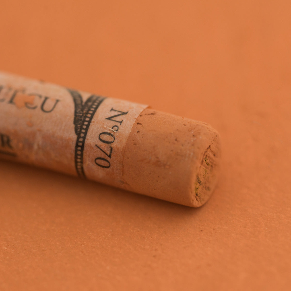 A close-up of a Sennelier extra soft pastel on a light brown background with the colour information printed on the paper wrap.