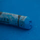 A close-up of a blue Sennelier extra soft pastel on the same coloured background, with the colour information printed on the paper wrap.