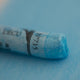 A close-up of a blue Sennelier extra soft pastel on the same coloured background, with the colour information printed on the paper wrap.