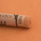 A close-up of a Sennelier extra soft pastel on a light brown background with the colour information printed on the paper wrap.