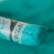 A close-up of a green Sennelier extra soft pastel. on the same coloured background, with the colour information printed on the paper wrap.