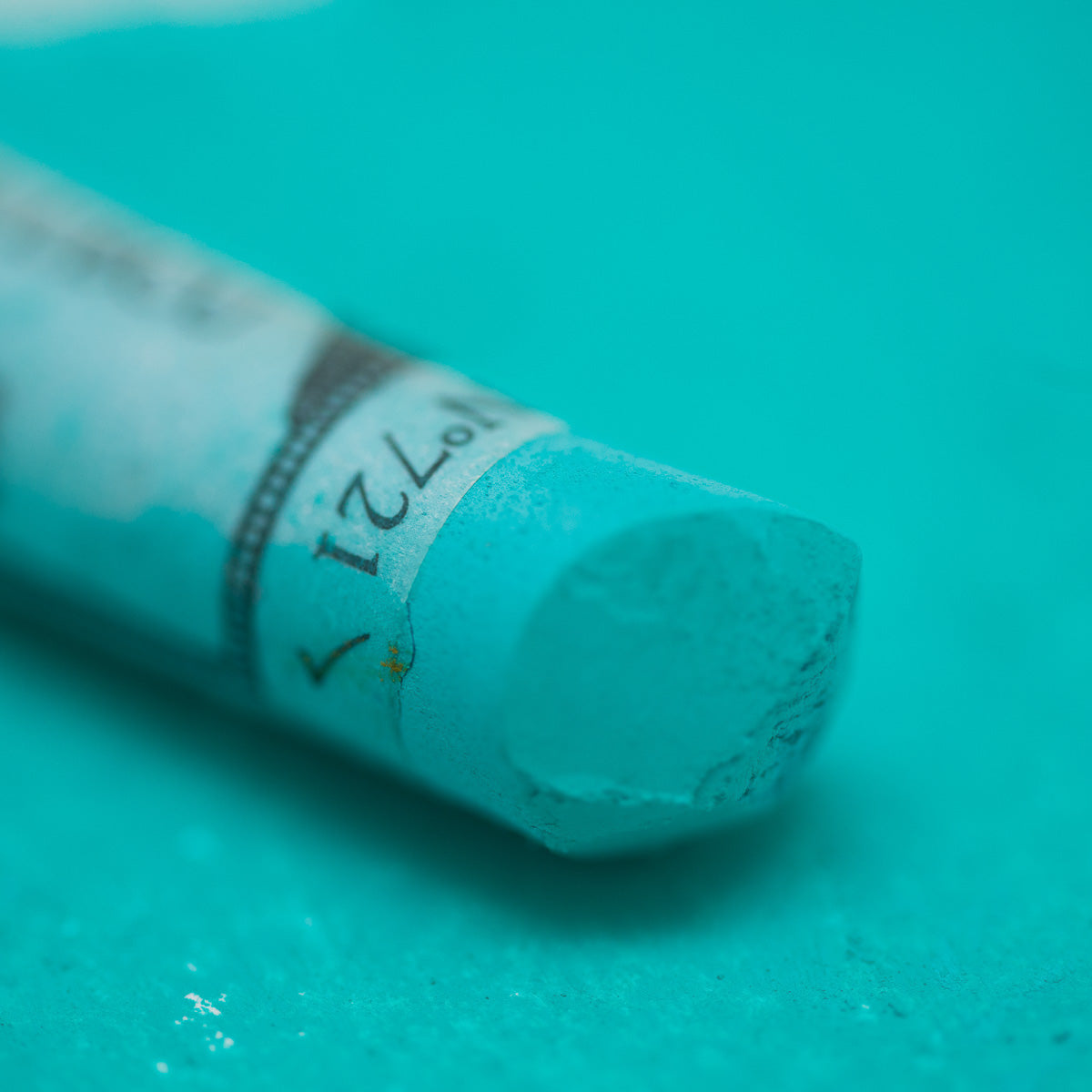 A close-up of a green Sennelier extra soft pastel. on the same coloured background, with the colour information printed on the paper wrap.
