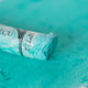 A close-up of a green Sennelier extra soft pastel. on the same coloured background, with the colour information printed on the paper wrap.