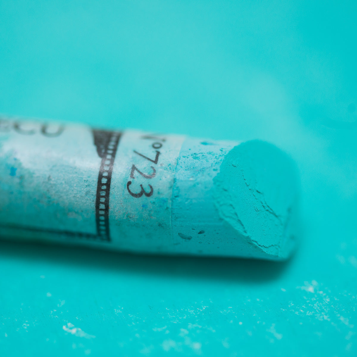 A close-up of a green Sennelier extra soft pastel. on the same coloured background, with the colour information printed on the paper wrap.