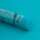 A close-up of a green Sennelier extra soft pastel. on the same coloured background, with the colour information printed on the paper wrap.